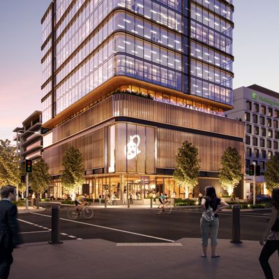 An artist’s impression of the lower floors of 50 First Avenue viewed from across the street at dusk, showing the entrance with a large, multi-storey curved glass feature section above the doors containing an abstract art piece and the surrounding the modern façade. The well-lit ground floor interior is visible showing the entrance lobby. Several tall trees line the neighbouring street with pedestrians walking by along the footpaths and cyclists riding along the street.