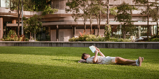 A person laying on the grass reading a book in the town square at Maroochydore City Centre.
